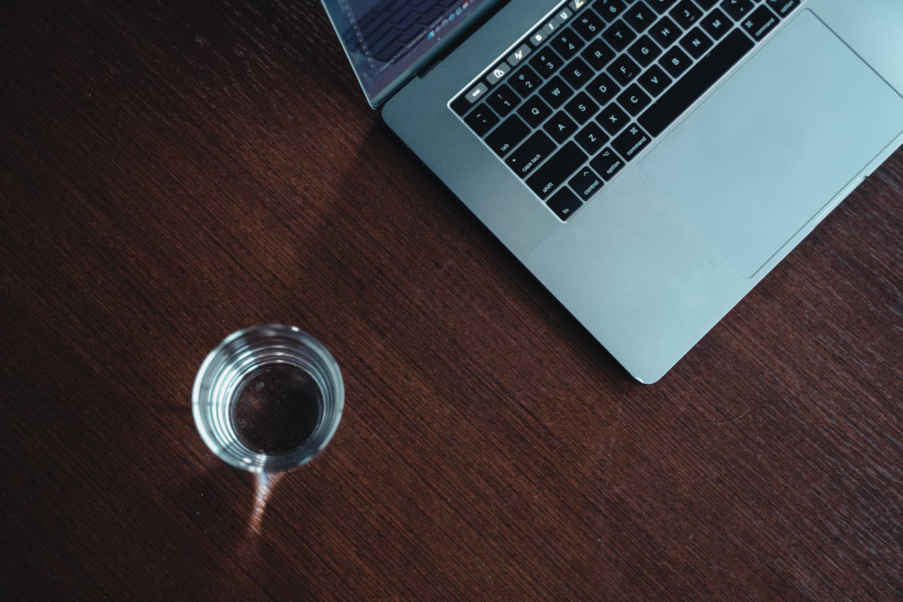 our-story-02 A modern workspace featuring a laptop and a glass of water on a wooden desk.